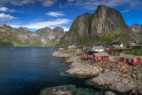 从 Hamnøy 桥望向海边红色渔屋，背景是陡峭的 Festhæltinden 山峰