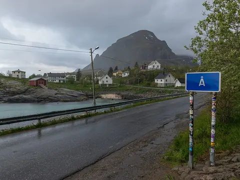 Å 村入口道路旁的蓝色 Å 字牌，远处是海湾、白色房屋与山峰